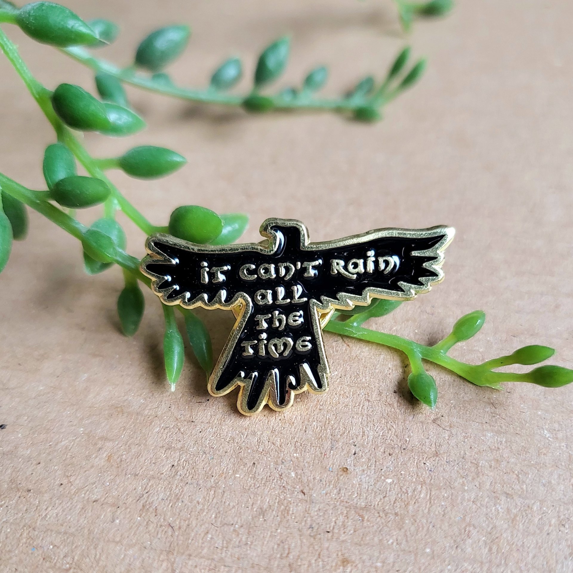 The Crow enamel pin badge, the crow movie black crow with the text 'it can't rain all the time' in gold. The crow film quote pin badge.