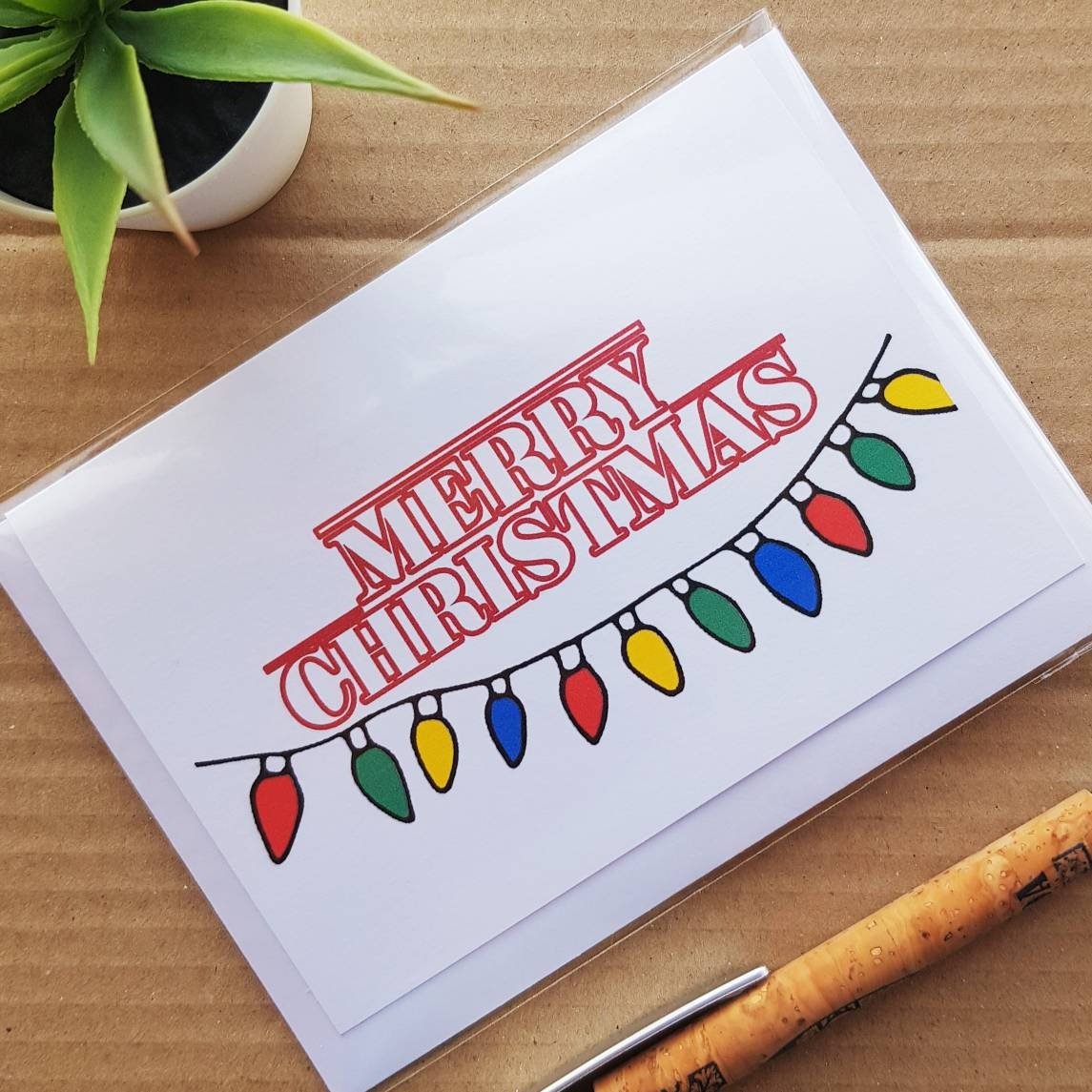 Cute Stranger Things Christmas card, front reads Merry Christmas in Stranger things font with Stranger things lights